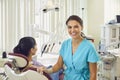 Smiling woman dentist at her office near the patient in the dental chair looking at the camera. Royalty Free Stock Photo