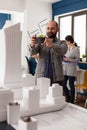 Smiling design architect holding smartphone to photograph desk with architectural model