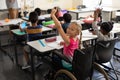 Smiling disable schoolgirl looking at camera and raising hand in classroom Royalty Free Stock Photo