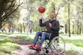 Smiling disabled man twirls basketball ball on his finger while sitting in wheelchair in park Royalty Free Stock Photo