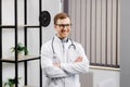 Smiling doctor posing with arms crossed in the office. Man is wearing a stethoscope and glasses. Medical staff on the workplace Royalty Free Stock Photo