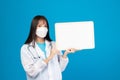 Smiling doctor wearing face mask holding blank banner or card with stethoscope on blue background Royalty Free Stock Photo