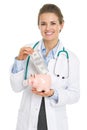 Smiling doctor woman putting dollars banknote in piggy bank