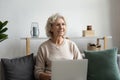 Smiling dreamy mature woman sitting with laptop on cozy couch Royalty Free Stock Photo