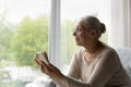 Smiling dreamy middle aged woman in glasses using cellphone.