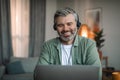 Smiling elderly european man with beard in headphones looks at laptop, talk with client, watch video lesson Royalty Free Stock Photo