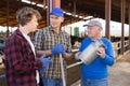 Smiling elderly farmer friendly chatting with son and grandson near stall with cows