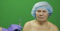 Smiling elderly female lady in protective hat scared of syringe with medicines