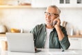 Smiling Elderly Gentleman Using Laptop And Talking On Cellphone In Kitchen Royalty Free Stock Photo