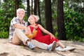 Smiling elderly lady eating apple sitting on sand near her husband