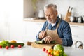 Smiling elderly man in apron cooking vegetable meal in kitchen Royalty Free Stock Photo