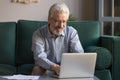 Smiling elderly man using laptop browsing internet at home