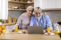 Smiling Elderly Spouses Relaxing With Laptop While Having Breakfast In Kitchen Royalty Free Stock Photo