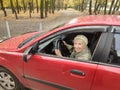 The smiling elderly woman in a red jacket at the wheel of the car