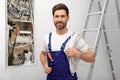 Smiling electrician with wires near open fuse box indoors