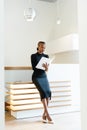 Smiling elegant business woman wearing black dress and beige shoes in light office looking at her agenda, full length portrait Royalty Free Stock Photo