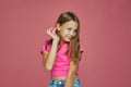 Smiling embarrassed shy caucasian child girl fixing her hair posing on pink studio background. Children& x27;s fashion