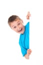 Smiling emotional positive teenager boy in bright blue t-shirt and posing behind a white panel isolated on white background. Place