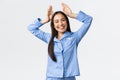 Smiling enthusiastic cute asian girl in blue pajamas showing bunny ears gesture over head, feeling playful and upbeat
