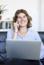 Entrepreneur woman wearing blue shirt working with a laptop sitting on a couch at home Royalty Free Stock Photo