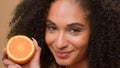 Smiling ethnic model girl African American woman hold half healthy orange fruit shake head with curly hair curls Royalty Free Stock Photo