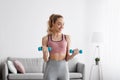 Smiling european beautiful young blonde woman strength exercising with dumbbells at home