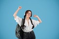 Smiling european girl with pigtails in glasses with backpack in wireless headphones dances, listen music Royalty Free Stock Photo