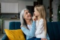 Smiling european old grandmother hugs small granddaughter, touches nose, enjoy free time