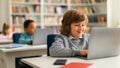 Smiling european schoolboy sitting at desk in front of laptop in classroom, typing or doing homework online, panorama