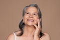 Smiling european senior lady with gray hair touches face with hand, looks at empty space Royalty Free Stock Photo