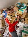 smiling european teen boy carrying pile of sorted waste paper next to heap of used paper.