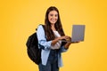 Smiling european teen student woman with backpack, typing on laptop