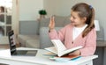 Smiling european teenager girl doing homework and reading book, waving hand at camera computer Royalty Free Stock Photo