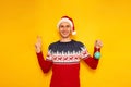 smiling, excited man in Christmas sweater with reindeer, red Santa Claus hat holds Christmas tree toy in his hand and Royalty Free Stock Photo