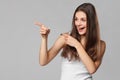 Smiling excited woman showing finger on copy space for product or text, isolated over grey background