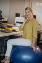 Smiling executive talking on mobile phone while sitting on exercise ball