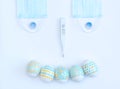 Smiling face made of decorated Easter eggs, medical face mask and thermometer on white background. Happy Easter during quarantine