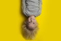 Smiling fair-haired boy hanging upside down on yellow background