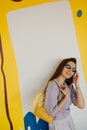 Smiling fair-skinned young woman in sunglasses straightens hair while standing against colorful wall Royalty Free Stock Photo