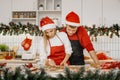 Smiling family couple wearing santa hats, decorating gingerbread Christmas cookies standing at table in modern kitchen, preparing Royalty Free Stock Photo