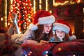 Smiling family mother and daughter in santas hats and pajamas watching funny video or choosing gifts on digital tablet