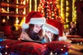 Smiling family mother and daughter in santas hats and pajamas watching funny video or choosing gifts on digital tablet