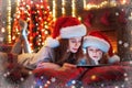 Smiling family mother and daughter in santas hats and pajamas watching funny video or choosing gifts on digital tablet