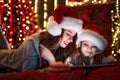 Smiling family mother and daughter in santas hats and pajamas watching funny video or choosing gifts on digital tablet