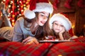 Smiling family mother and daughter in santas hats and pajamas watching funny video or choosing gifts on digital tablet Royalty Free Stock Photo