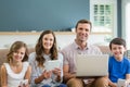 Smiling family using digital tablet, phone and laptop in living room at home Royalty Free Stock Photo