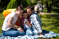 Smiling Family Watching Photo On Mobile Phone While Sitting On The Blanket In The Park.