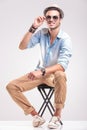 Smiling fashion man fixing his sunglasses while sitting Royalty Free Stock Photo