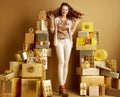 Smiling fashion-monger among 2 piles of golden gifts rejoicing