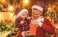 Smiling father and his son in Santa`s hat open a Christmas gift present box. New Year tree and fire place at background Royalty Free Stock Photo